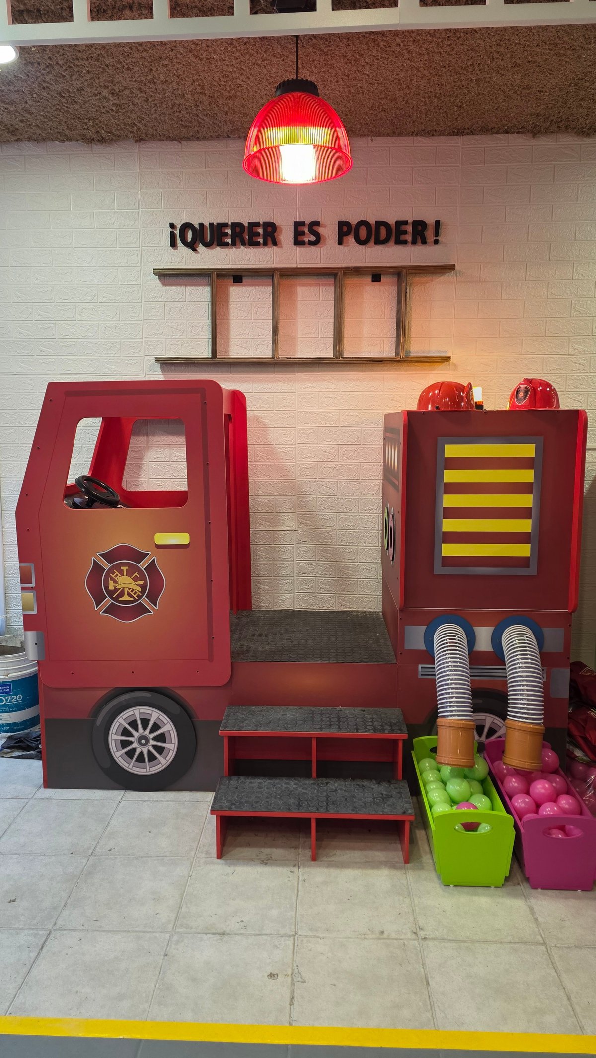 Camión de bomberos rojo con cartel ¡Querer es poder! y pelotas verdes y rosadas